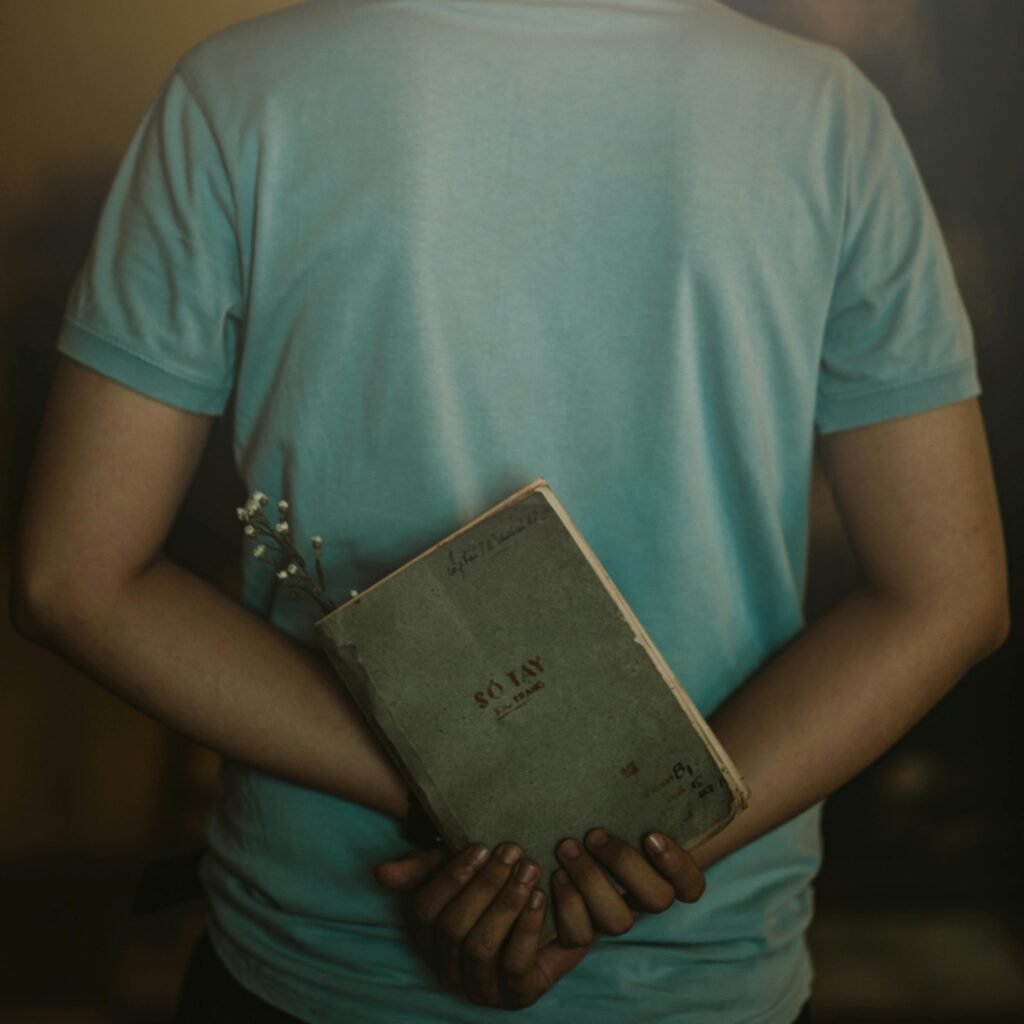 A person in a casual shirt holding a notebook and flowers behind their back, symbolizing contemplation.